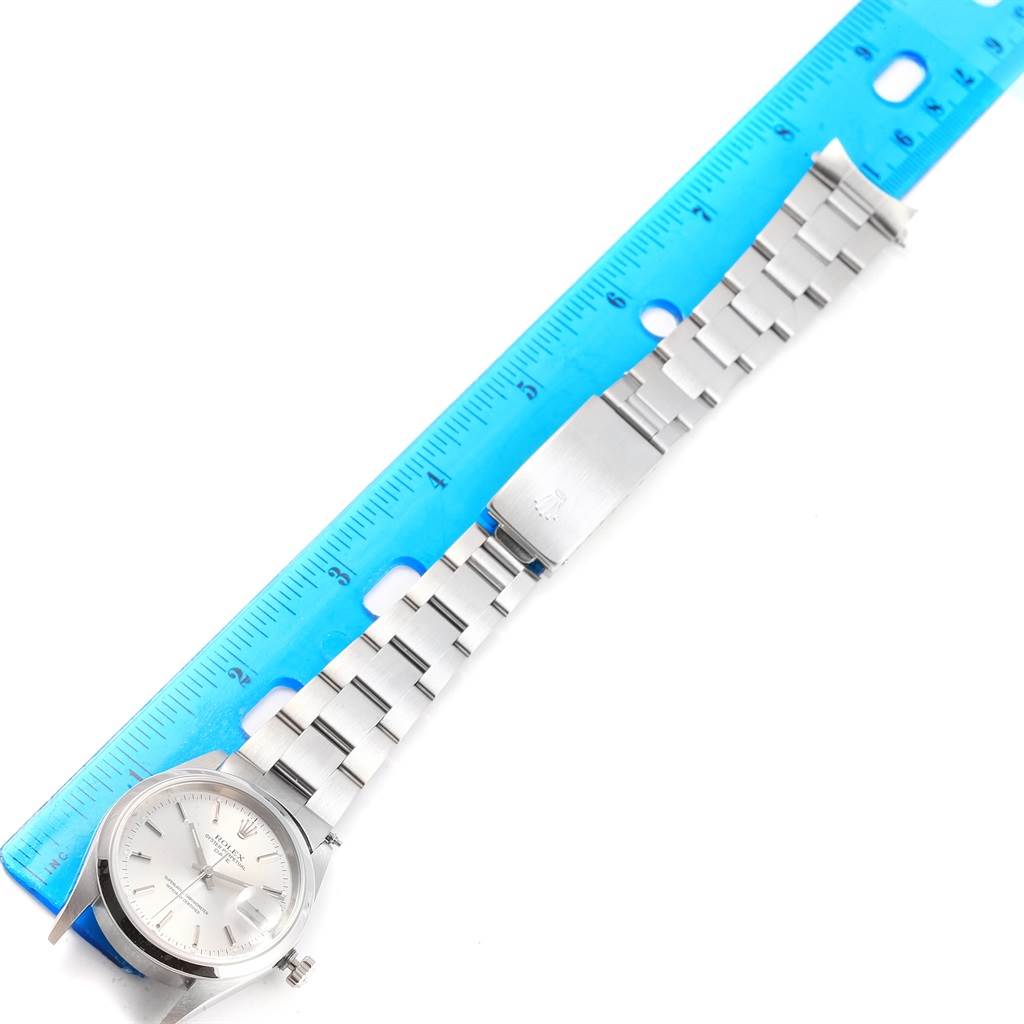 The image shows a Rolex Date 15200 Men's Stainless Steel Silver Dial 15200 Men's Stainless Steel Silver Dial model watch laid flat alongside a blue ruler, displaying its face and metal bracelet.