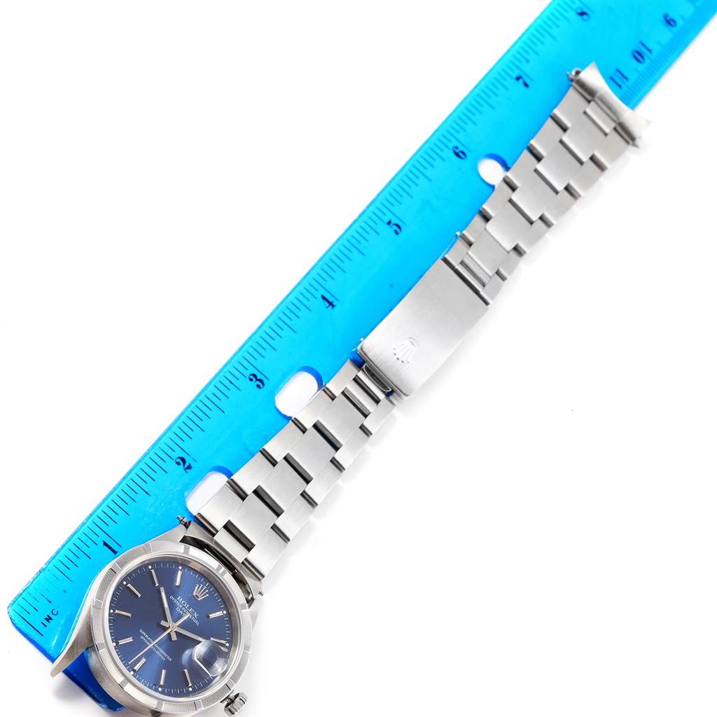 The Rolex Date 15210 Men's Stainless Steel Blue Dial 15210 Men's Stainless Steel Blue Dial watch is shown from a top-down angle, displaying the face, bracelet, and clasp alongside a blue ruler.