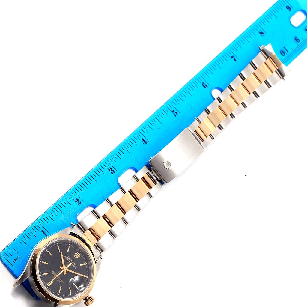 The image shows a Rolex Date 15203 Men's Steel and Gold (two tone) Black Dial 15203 Men's Steel and Gold (two tone) Black Dial model watch laying flat next to a ruler, displaying the face and strap.