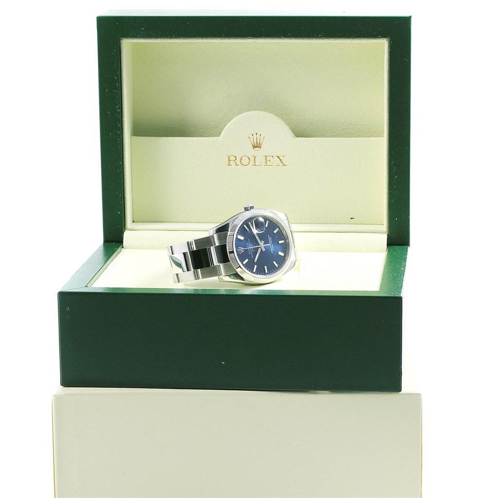 The Rolex Date 115210 Men's Stainless Steel Blue Dial 115210 Men's Stainless Steel Blue Dial watch is shown inside an open green and beige Rolex box, viewed from the front.