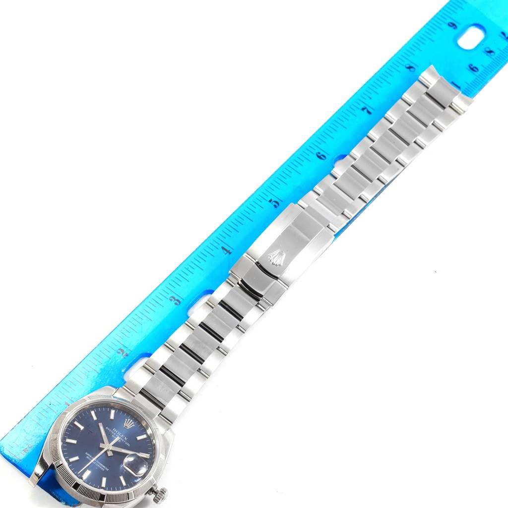 The image shows a Rolex Date 115210 Men's Stainless Steel Blue Dial 115210 Men's Stainless Steel Blue Dial model watch laid flat with a metallic band, alongside a blue ruler for scale.