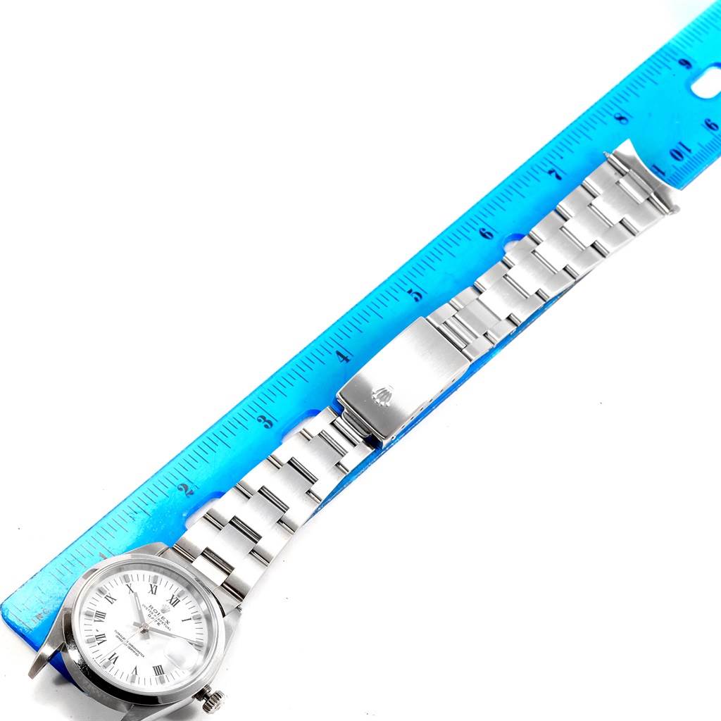 The Rolex Date 15200 Men's Stainless Steel White Dial 15200 Men's Stainless Steel White Dial watch is shown from an angled top view with a focus on the watch face, bracelet, and clasp alongside a blue ruler.