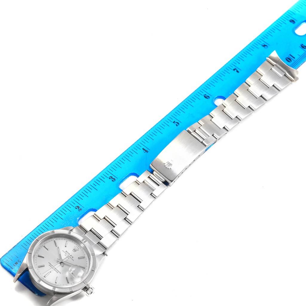 The image shows a Rolex Date 15210 Men's Stainless Steel Silver Dial 15210 Men's Stainless Steel Silver Dial model watch laid flat, highlighting its dial, bracelet, and clasp against a blue ruler.