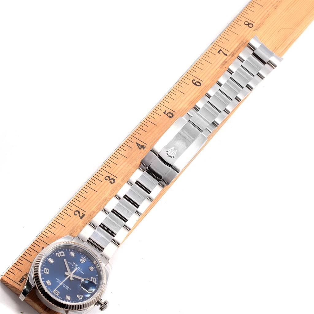 The image shows a Rolex Date 115234 Men's Stainless Steel Blue Dial 115234 Men's Stainless Steel Blue Dial watch laid flat next to a ruler, displaying the face and the full metal bracelet.