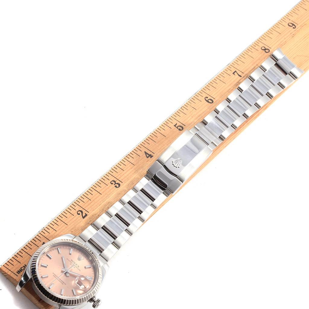 The image shows a Rolex Date 115234 Stainless Steel Pink Dial 115234 Stainless Steel Pink Dial model watch laid flat with its band extended next to a ruler for measurement.