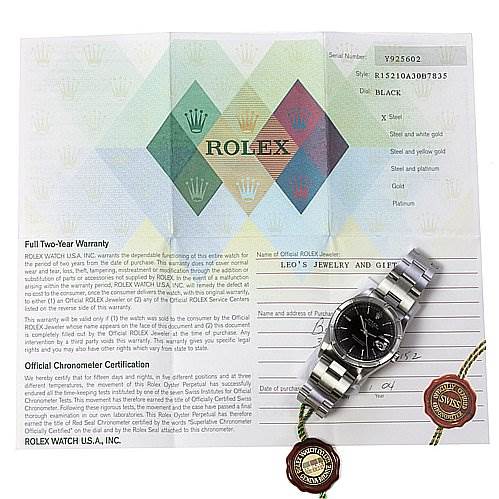The image shows a Rolex Date 15210 Men's Stainless Steel Black Dial 15210 Men's Stainless Steel Black Dial model watch with its warranty card and two tags. The watch is positioned face-up displaying its dial and bracelet.