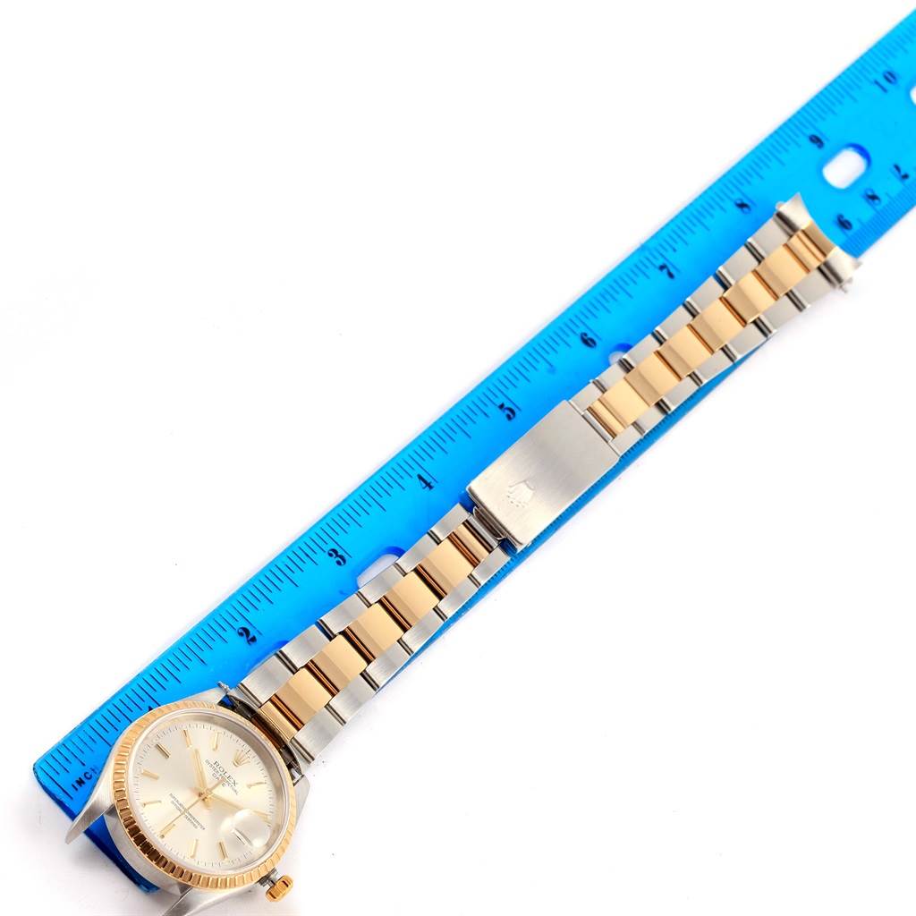 The watch, a Rolex Date 15223 Men's Steel and Gold (two tone) Silver Dial 15223 Men's Steel and Gold (two tone) Silver Dial model, is photographed from above alongside a blue ruler, showing its band and face.