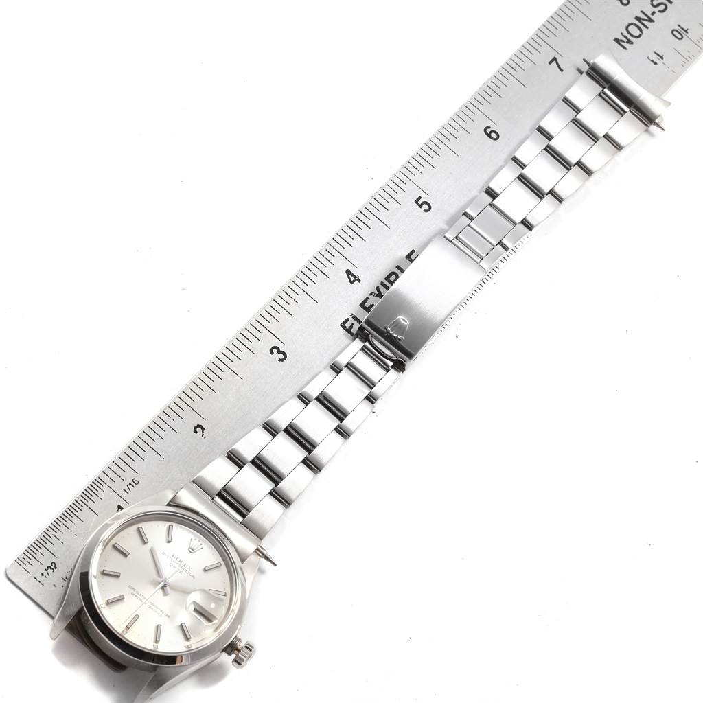 The image shows a Rolex Date 1500 Men's Stainless Steel Silver Dial 1500 Men's Stainless Steel Silver Dial model watch placed next to a ruler for measurement, focusing on the watch face and bracelet.