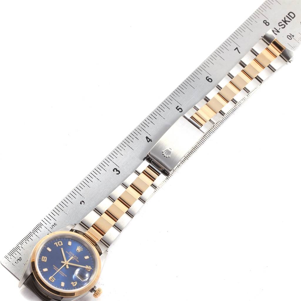 The image shows a Rolex Date 15203 Men's Steel and Gold (two tone) Blue Dial 15203 Men's Steel and Gold (two tone) Blue Dial model watch with a blue dial, gold bezel, and a two-tone metal bracelet next to a ruler.