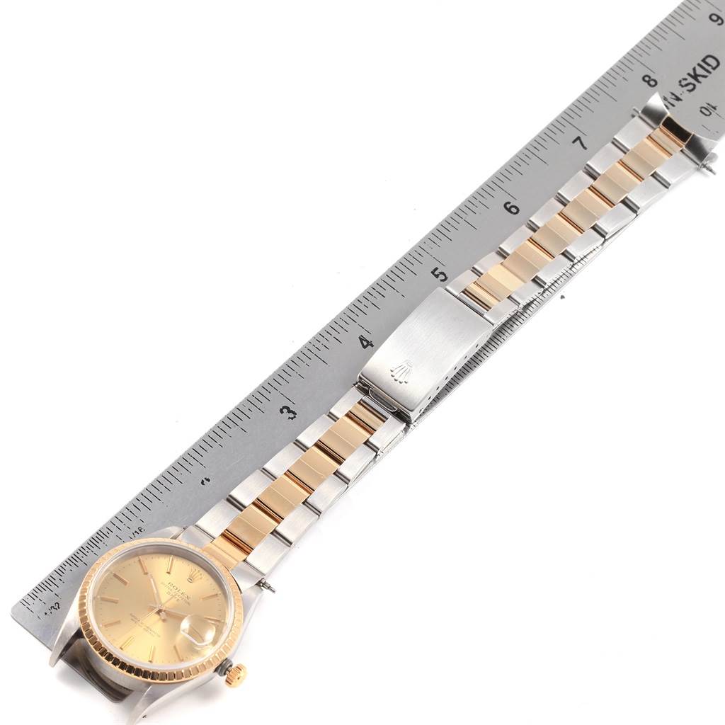 This image shows a Rolex Date 15223 Men's Steel and Gold (two tone) Champagne Dial 15223 Men's Steel and Gold (two tone) Champagne Dial model watch laid flat next to a ruler, highlighting its bracelet and face.