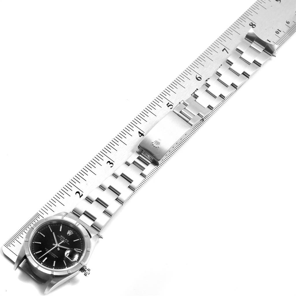 The image shows a top-down view of a Rolex Date 15210 Men's Stainless Steel Black Dial 15210 Men's Stainless Steel Black Dial watch, featuring its dial, case, and metal bracelet next to a ruler.