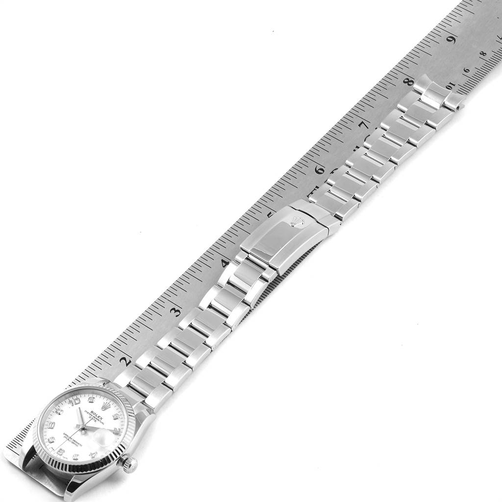 The image shows a Rolex Date 115234 Men's Stainless Steel White Dial 115234 Men's Stainless Steel White Dial model watch from an overhead angle, displaying its bracelet and clasp alongside a ruler.