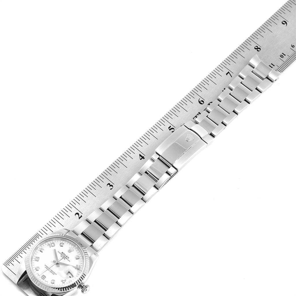 The image shows a Rolex Date 115234 Men's Stainless Steel White Dial 115234 Men's Stainless Steel White Dial watch with a ruler along its bracelet, capturing the watch face and closed clasp.