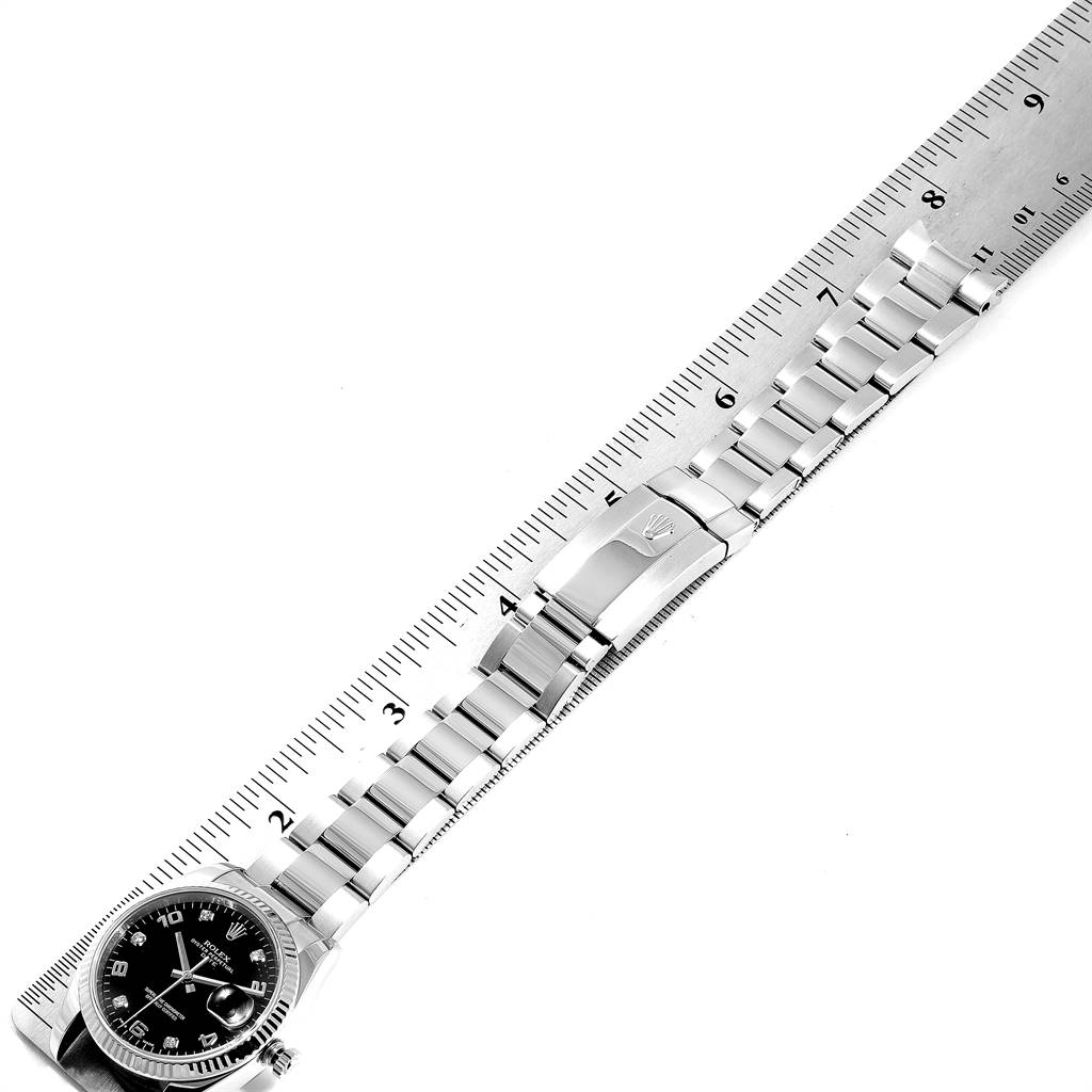 This image shows the Rolex Date 115234 Men's Stainless Steel Black Dial 115234 Men's Stainless Steel Black Dial model watch from an aerial angle, focusing on the bracelet and clasp, with a ruler for measurement.