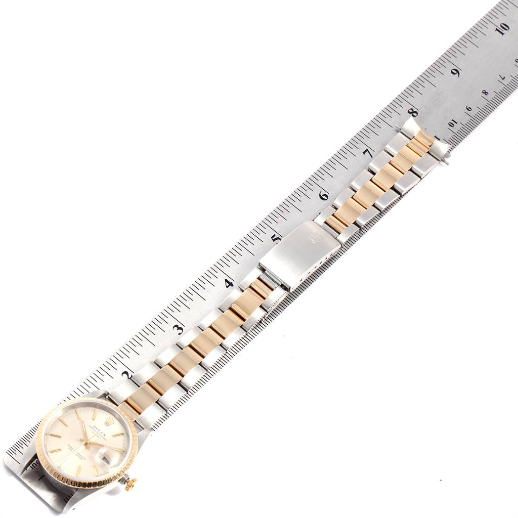 The Rolex Date 15223 Men's Steel and Gold (two tone) Silver Dial 15223 Men's Steel and Gold (two tone) Silver Dial model watch is shown horizontally with its full bracelet and clasp visible next to a ruler.