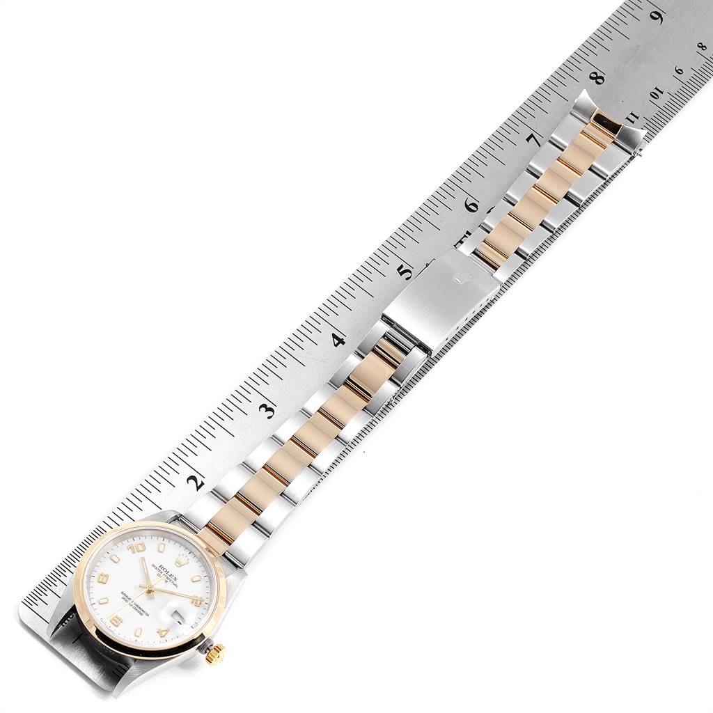 The image shows a Rolex Date 15203 Men's Steel and Gold (two tone) White Dial 15203 Men's Steel and Gold (two tone) White Dial model watch laying horizontally on a ruler, displaying its face, strap, and clasp.