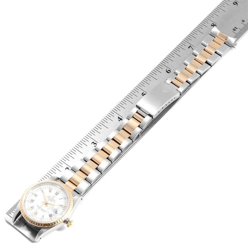 The Rolex Date 15223 Men's Steel and Gold (two tone) White Dial 15223 Men's Steel and Gold (two tone) White Dial model watch is shown from a top-down angle, highlighting its face, bezel, crown, and two-tone bracelet next to a ruler.