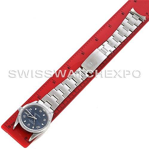 The image shows a side view of a Rolex Date 15210 Men's Stainless Steel Blue Dial 15210 Men's Stainless Steel Blue Dial model watch placed against a red ruler, showcasing its bracelet and clasp.