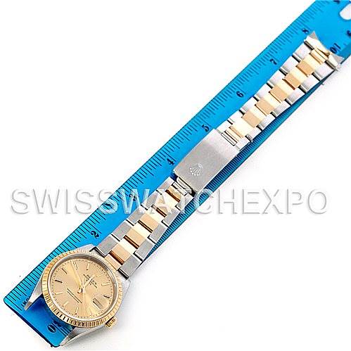 The Rolex Date 15223 Men's Steel and Gold (two tone) Champagne Dial 15223 Men's Steel and Gold (two tone) Champagne Dial model watch is shown lying flat, featuring its watch face, band, and clasp alongside a blue measuring ruler.