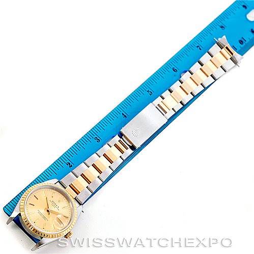 The image shows a Rolex Date 15223 Men's Steel and Gold (two tone) Champagne Dial 15223 Men's Steel and Gold (two tone) Champagne Dial model watch laying flat next to a blue ruler, highlighting the full bracelet and face of the watch.