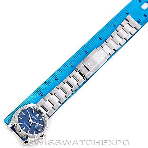 This image shows a Rolex Date 115210 Men's Stainless Steel Blue Dial 115210 Men's Stainless Steel Blue Dial model watch laid flat next to a blue ruler, displaying the watch face and bracelet from a top-down angle.