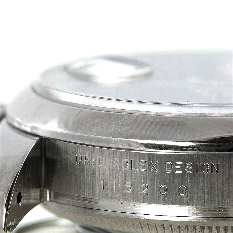 The image shows a close-up side view of the case and bezel of the Rolex Date 115200 Men's Stainless Steel Blue Dial 115200 Men's Stainless Steel Blue Dial model watch with the serial number visible.