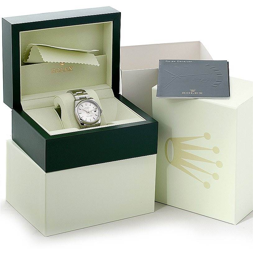 The image shows a Rolex Date 115200 Men's Stainless Steel Silver Dial 115200 Men's Stainless Steel Silver Dial model watch in its open box, alongside a card and an outer box with a cleaning cloth.