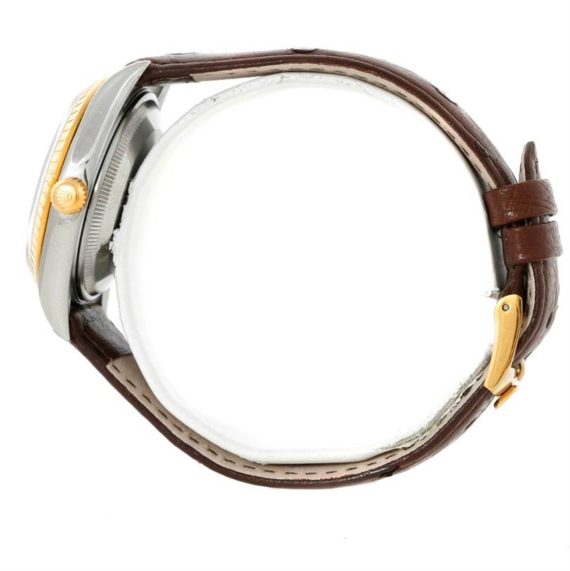 This side view of the Rolex Date 15203 Men's Steel and Gold (two tone) Grey Dial 15203 Men's Steel and Gold (two tone) Grey Dial model shows the crown, bezel, case, and leather strap with its buckle.