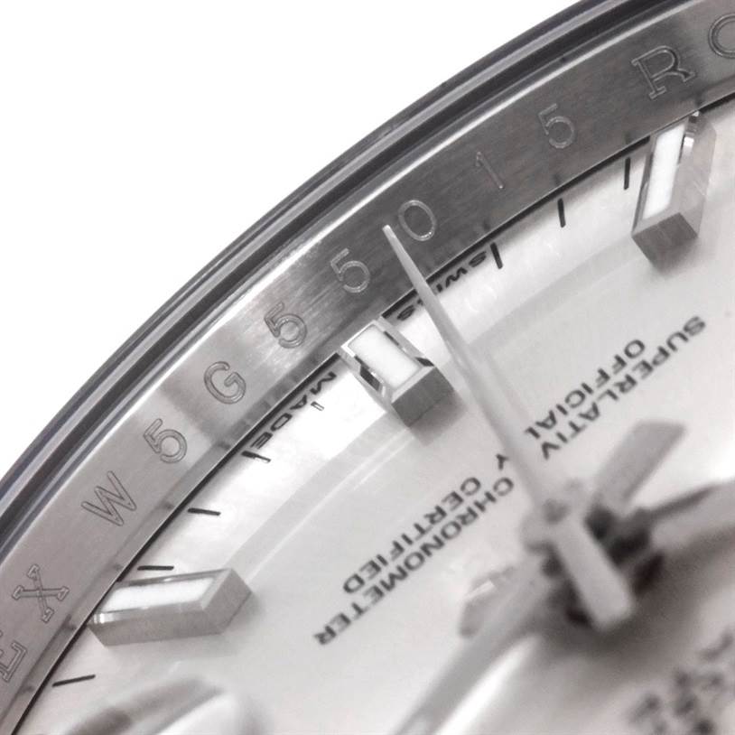 This close-up image of the Rolex Date 115234 Men's Stainless Steel Silver Dial 115234 Men's Stainless Steel Silver Dial model watch displays the etched serial number, inner bezel, hour markers, and part of the dial.