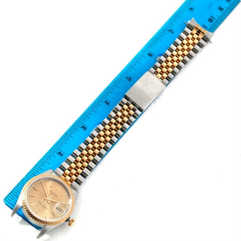 This image shows a Rolex Date 15223 Men's Steel and Gold (two tone) Champagne Dial 15223 Men's Steel and Gold (two tone) Champagne Dial model watch positioned alongside a blue ruler, displaying the face, bezel, crown, and bracelet.