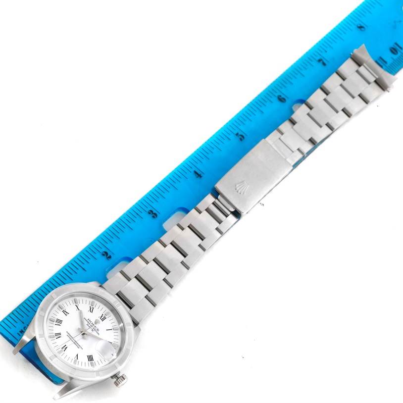 The Rolex Date 15210 Men's Stainless Steel White Dial 15210 Men's Stainless Steel White Dial watch is displayed from a top-down angle, showing the dial, case, bracelet, and clasp alongside a blue ruler.