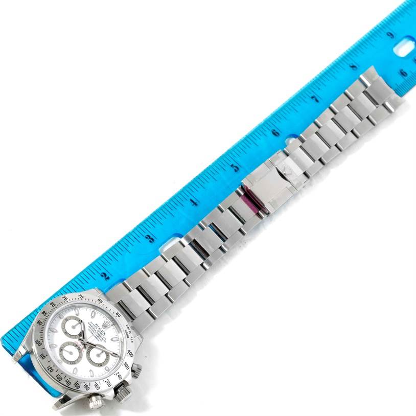 The image shows a Rolex Daytona 116520 Men's Stainless Steel White Dial 116520 Men's Stainless Steel White Dial watch laid flat beside a blue ruler, highlighting the face, dial, bracelet, and clasp.