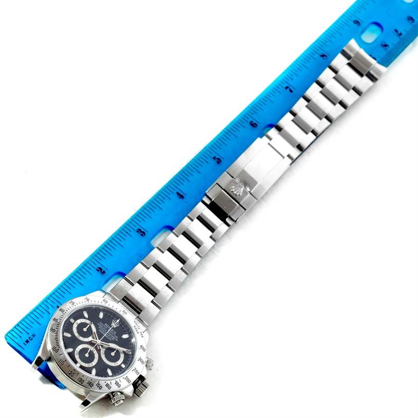 The image shows a top-down view of a Rolex Daytona 116520 Men's Stainless Steel Black Dial 116520 Men's Stainless Steel Black Dial watch, including its dial, bezel, and metal bracelet next to a ruler.