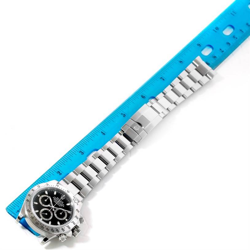 The image shows a Rolex Daytona 116520 Men's Stainless Steel Black Dial 116520 Men's Stainless Steel Black Dial watch laid flat beside a blue ruler, with the watch face, bracelet, and clasp visible.