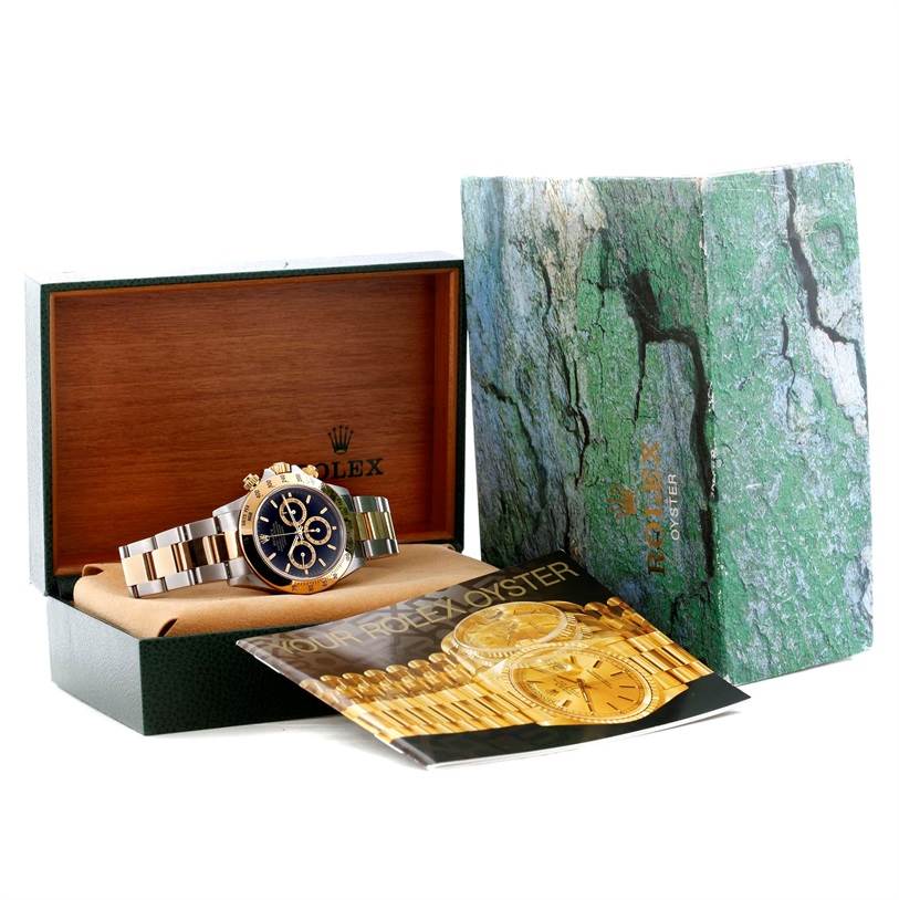 The image shows a Rolex Daytona 16523 Men's Steel and Gold (two tone) Black Dial 16523 Men's Steel and Gold (two tone) Black Dial watch at an angled side view, along with its open box and manual.