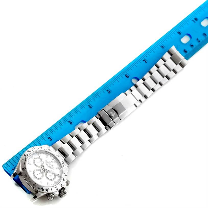 The image shows a Rolex Daytona 116520 Men's Stainless Steel White Dial 116520 Men's Stainless Steel White Dial watch laid flat alongside a ruler, displaying its face, bezel, and bracelet.