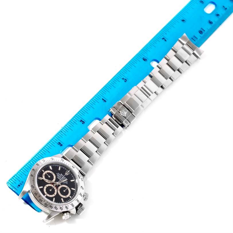 The Rolex Daytona 16520 Men's Stainless Steel Black Dial 16520 Men's Stainless Steel Black Dial watch is shown with its full metal bracelet and clasp aligned beside a blue ruler for size reference.