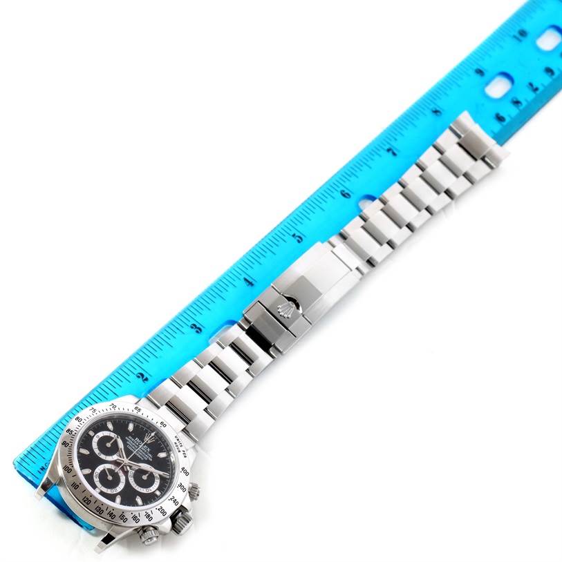 The image shows a top-down view of a Rolex Daytona 116520 Men's Stainless Steel Black Dial 116520 Men's Stainless Steel Black Dial watch with a metal bracelet placed next to a blue ruler for scale.