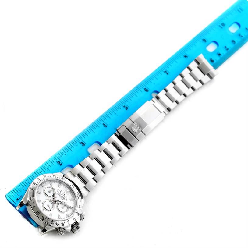 This image shows a top-down view of a Rolex Daytona 116520 Men's Stainless Steel White Dial 116520 Men's Stainless Steel White Dial watch, including its face and metal bracelet, adjacent to a blue ruler.