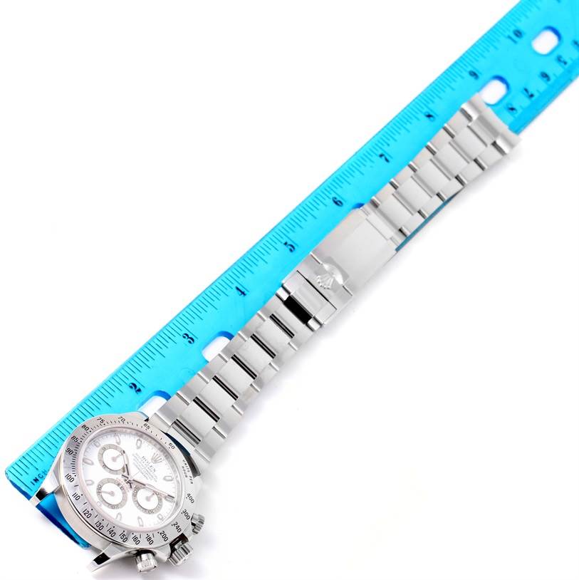The image shows the full length of the Rolex Daytona 116520 Men
s Stainless Steel White Dial 116520 Men
s Stainless Steel White Dial watch placed next to a blue ruler for size reference.