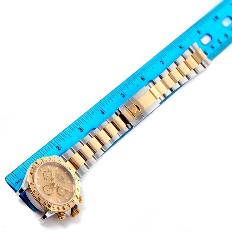 The image shows a Rolex Daytona 116523 Men's Steel and Gold (two tone) Champagne Dial 116523 Men's Steel and Gold (two tone) Champagne Dial watch and its two-tone bracelet, aligned with a ruler for scale.