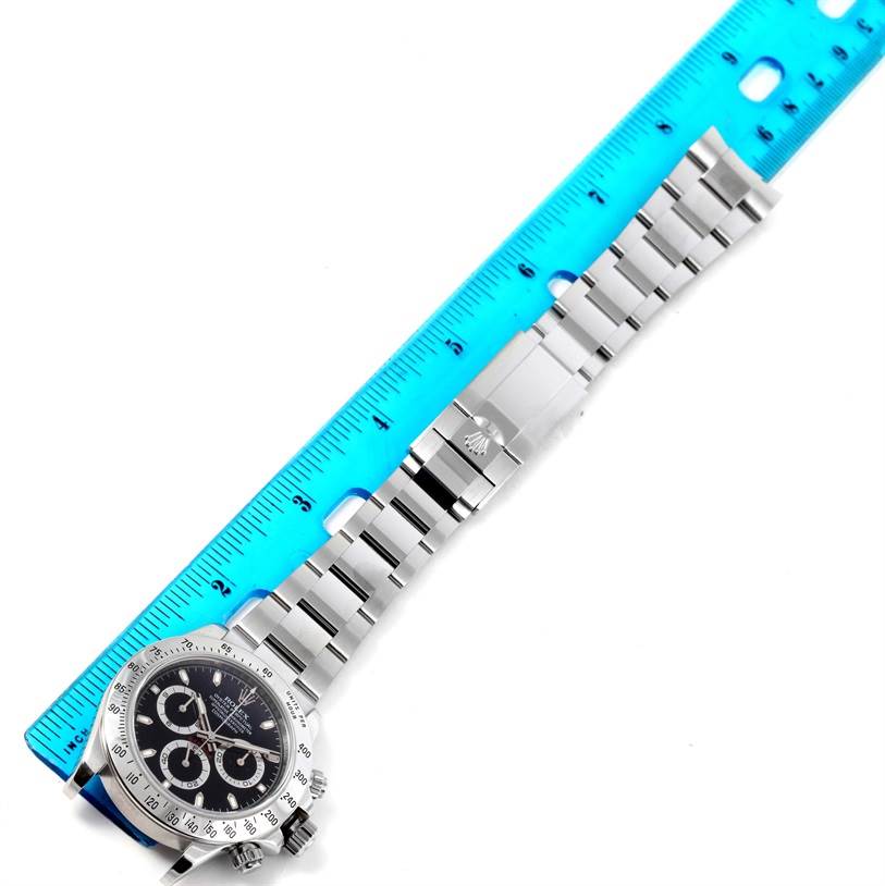 The Rolex Daytona 116520 Men's Stainless Steel Black Dial 116520 Men's Stainless Steel Black Dial watch is shown from a top-down angle, displaying its face, bracelet, and clasp alongside a blue ruler for measurement.