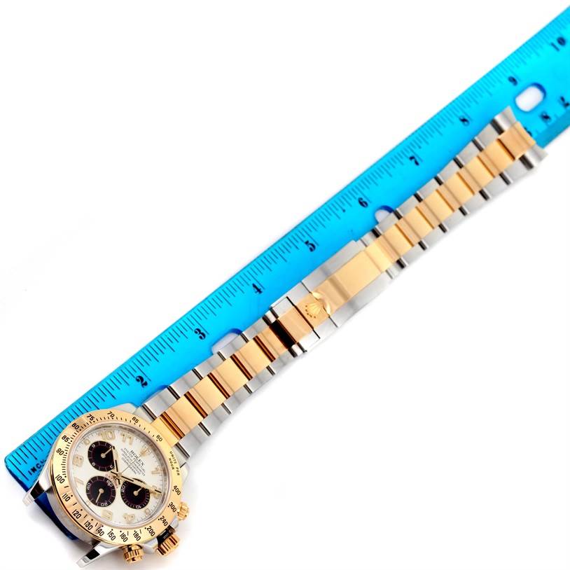 A Rolex Daytona 116523 Men's Steel and Gold (two tone) White Dial 116523 Men's Steel and Gold (two tone) White Dial watch is shown from the top view, displaying its bracelet and dial with a blue ruler for scale.