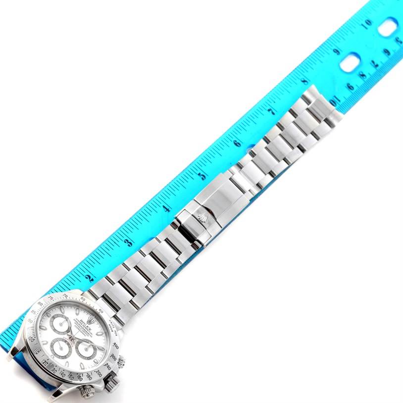 The image shows a Rolex Daytona 116520 Men's Stainless Steel White Dial 116520 Men's Stainless Steel White Dial watch laid flat with a blue ruler beside it, revealing the face, bezel, and full bracelet.