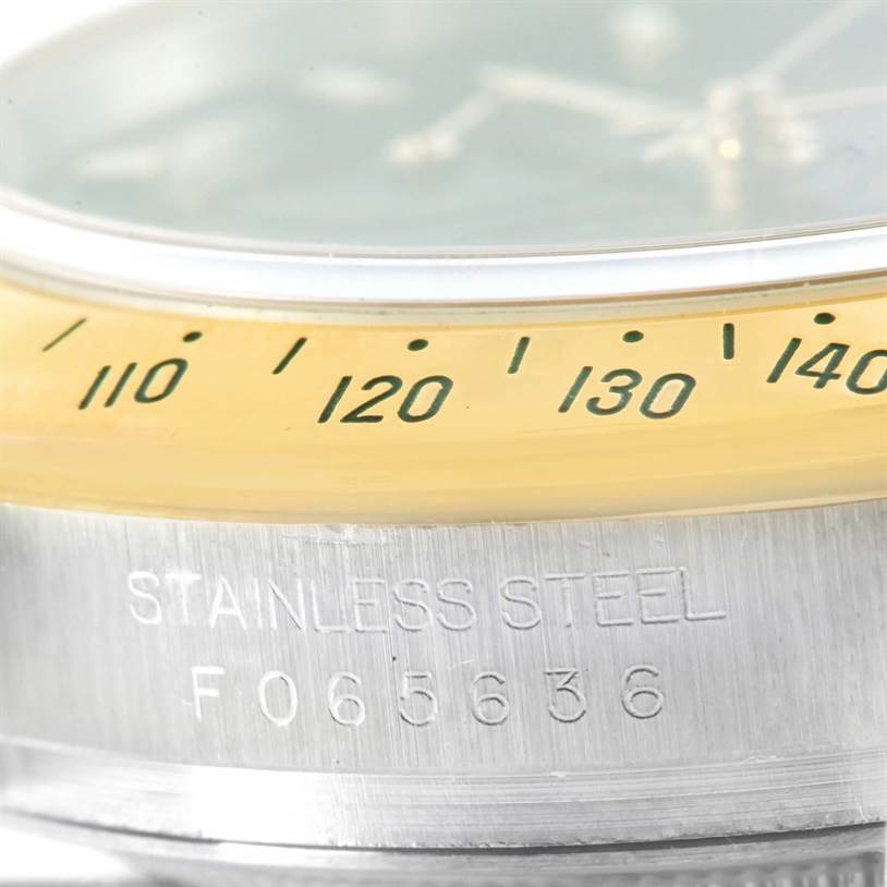 This close-up image of a Rolex Daytona 116523 Men's Steel and Gold (two tone) Black Dial 116523 Men's Steel and Gold (two tone) Black Dial watch shows the stainless steel case with serial number and the edge of the bezel with tachymeter markings.