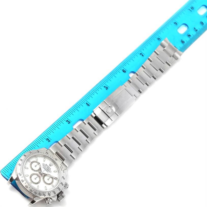 The image shows a Rolex Daytona 116520 Men's Stainless Steel White Dial 116520 Men's Stainless Steel White Dial watch lying flat with its full stainless steel bracelet and a blue measuring ruler beside it.