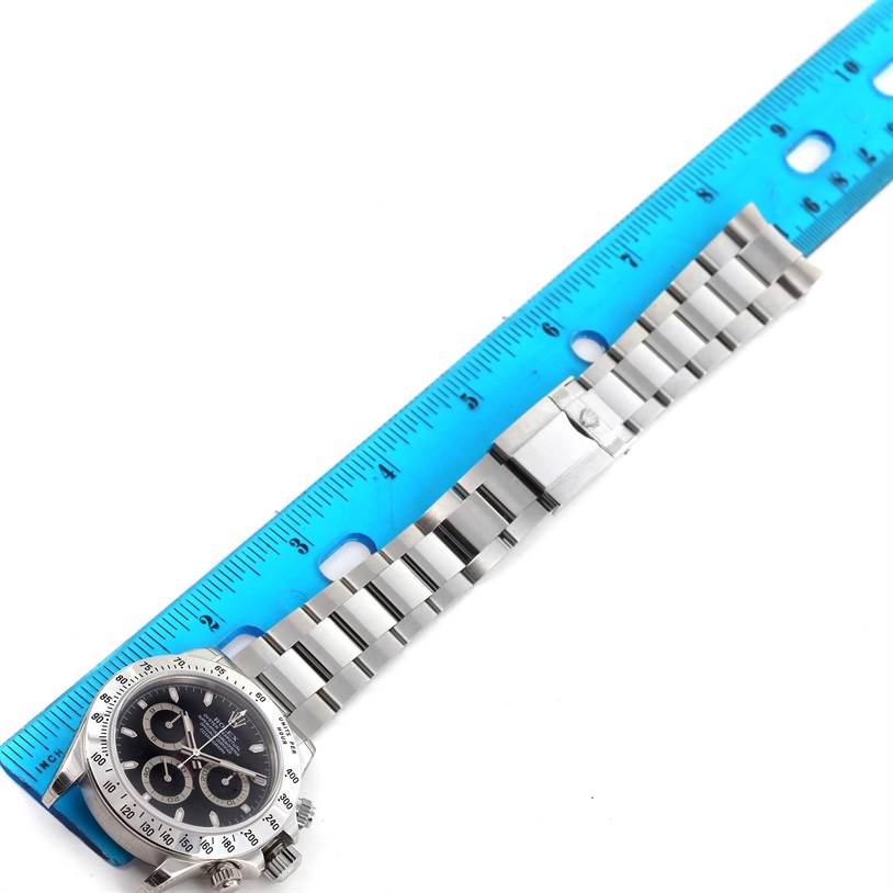 The image shows a Rolex Daytona 116520 Men
s Stainless Steel Black Dial 116520 Men
s Stainless Steel Black Dial watch laid flat with a blue ruler placed above it, displaying the dial, bezel, and full bracelet.