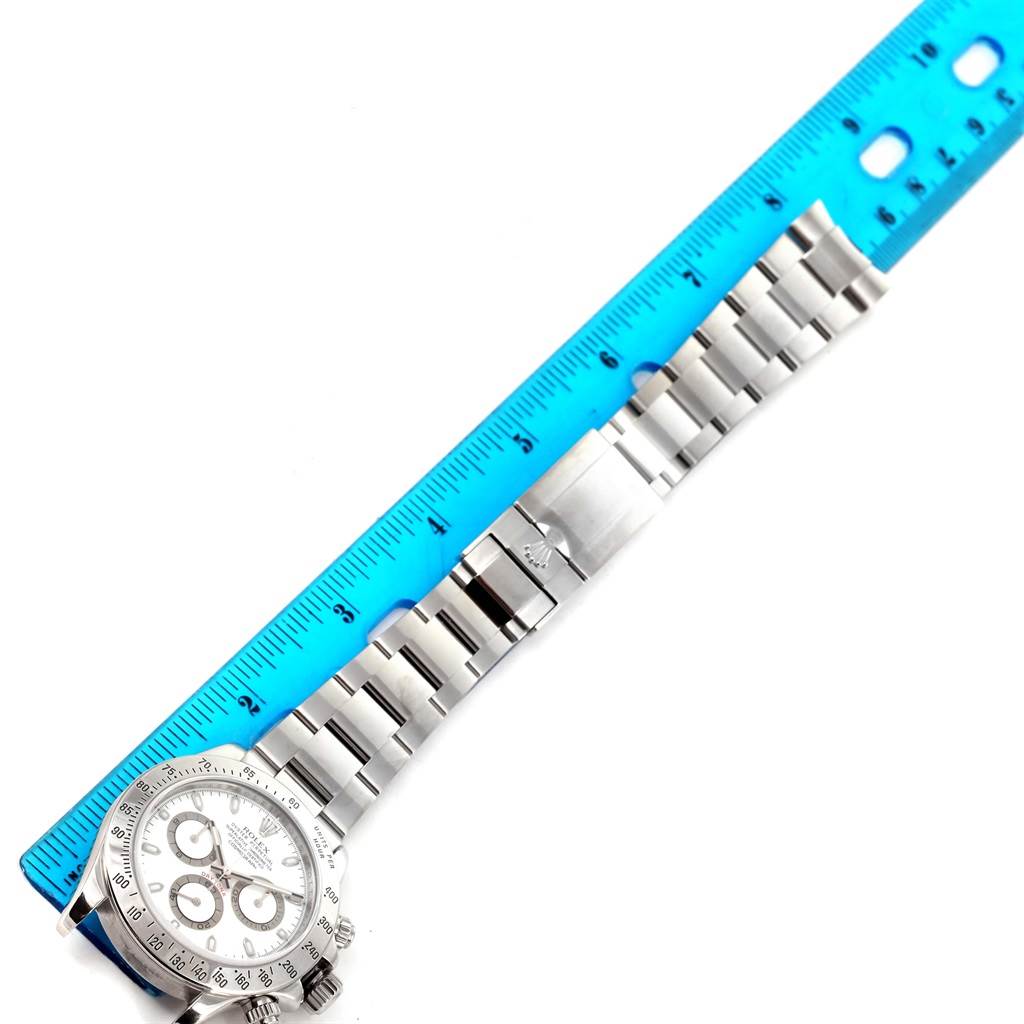 The image shows a Rolex Daytona 116520 Men
s Stainless Steel White Dial 116520 Men
s Stainless Steel White Dial watch laid flat next to a blue ruler, displaying the face and metal bracelet from an overhead angle.