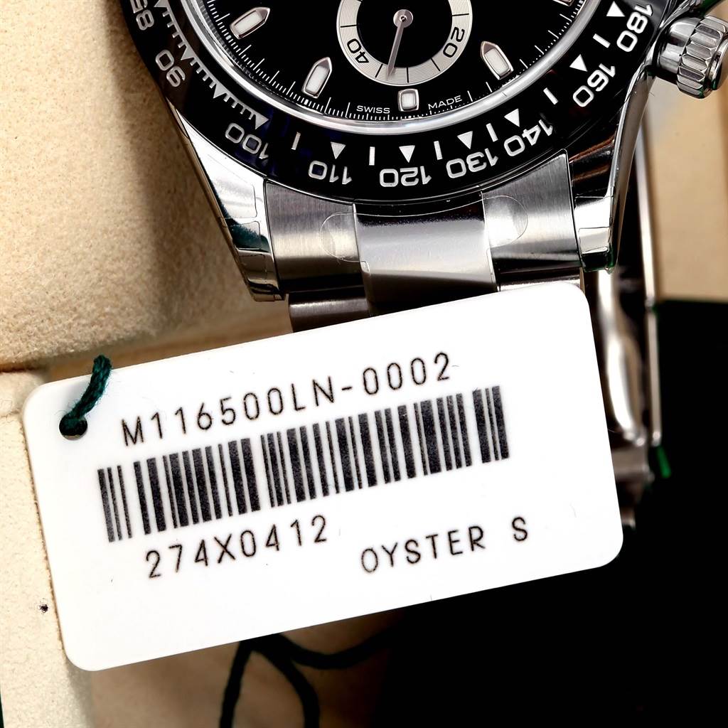 The image shows a close-up of the Rolex Daytona 116500 Men's Stainless Steel Black Dial 116500 Men's Stainless Steel Black Dial model knurled bezel, part of the dial, crown, and bracelet with a tag.
