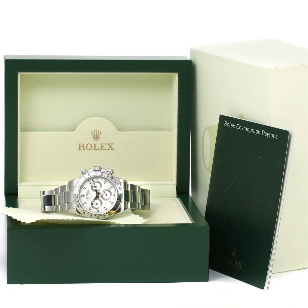 The image shows a Rolex Daytona 116520 Men's Stainless Steel White Dial 116520 Men's Stainless Steel White Dial watch in its case, with a manual on the side, viewed from the front.